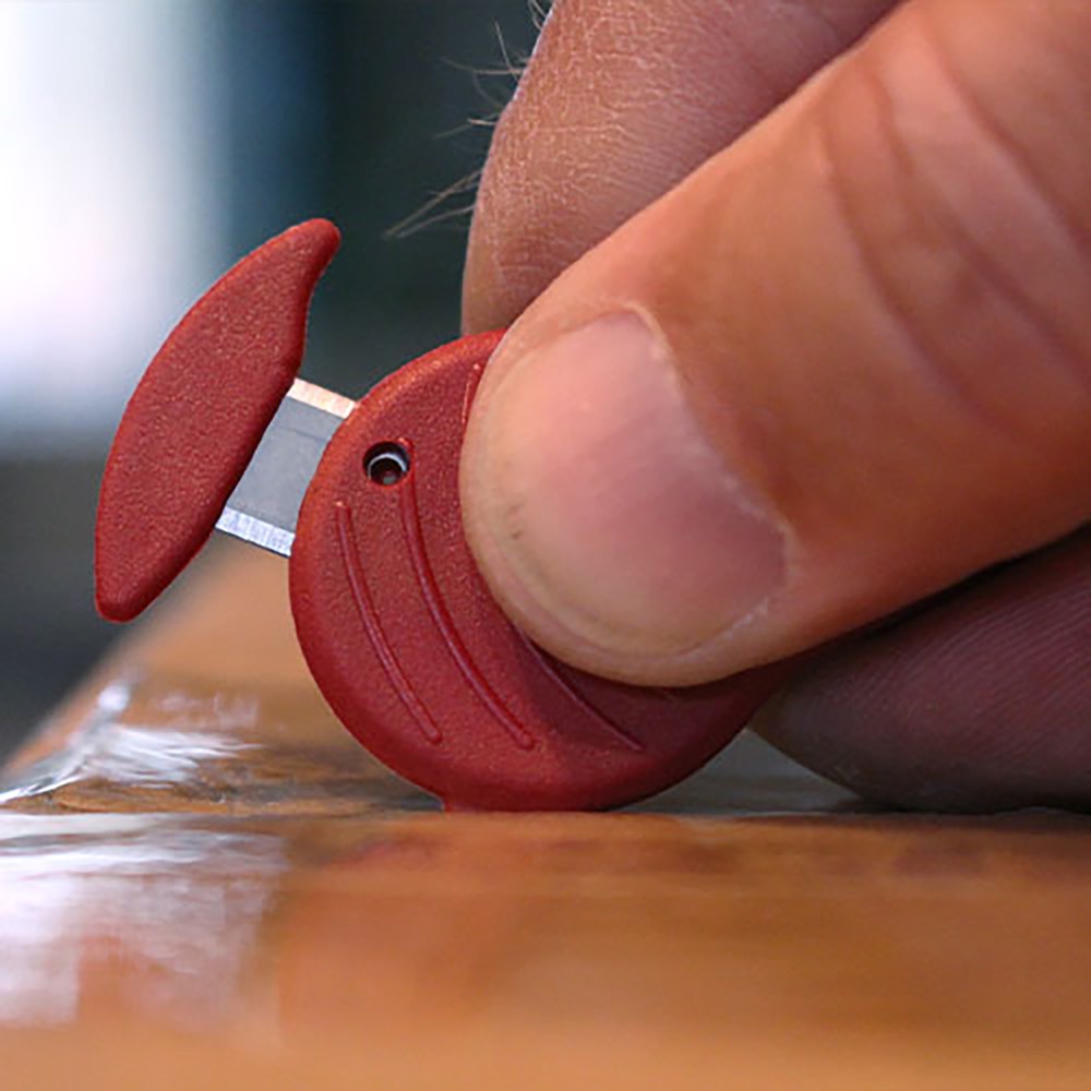 In-use photo: hand cutting along a table edge with the red ULTRA SAFE 48